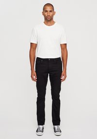 Melni slim-fit džinsi apvienoti ar baltu klasiska cnc kreklu un melniem sneakeriem. Audums izskatās gluds ar minimālu detalizāciju.