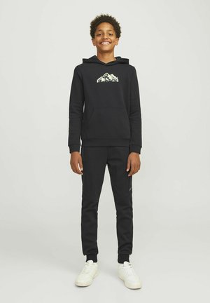 Haut à capuche en coton noir avec un graphique de montagne sur la poitrine, associé à un pantalon jogger noir assorti et des baskets blanches. Texture lisse, coupe décontractée.