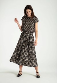 Bloemenpatroon in zwart en beige outfit met een losvallende top en een lange, vloeiende rok. De stof is lichtgewicht en glad, met een tailleband met trekkoorden.