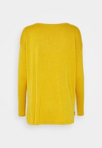 Gul tröja med lång ärm, vid halsringning och rak skärning. Texturerat tyg och subtila sidsömsdetaljer.