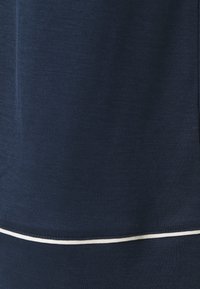 Námořnická modrá látka, hladký povrch, s bílým prošívaným okrajem na spodní části. Jednoduchý a jednolitý design bez vzorů nebo akcentů.