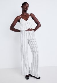 Top blanc court avec bordure froncée et détails en crochet, associé à un pantalon large rayé blanc. Des chaussures noires à pois complètent la tenue.