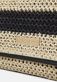 Torebka z plecionki słomianej z czarnymi i naturalnymi beżowymi paskami, prostokątny kształt oraz złotą blaszką z logo "ANNA FIELD". Teksturowana powierzchnia.