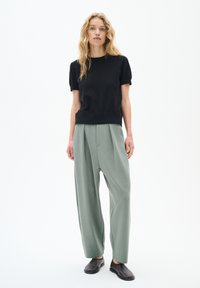 Top nero a maniche corte, pantaloni verdi salvia dal taglio morbido e dallo texture liscia, e scarpe nere senza lacci. Design semplice e minimalista.