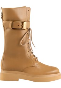 Tan leren combatboot met een vetersluiting aan de voorkant, ronde neus, stevige zool en een decoratieve gouden gesp rond de enkel. Gladde textuur, minimalistisch ontwerp.