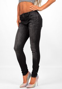 Jeans skinny neri realizzati in denim con una texture liscia. Presentano una chiusura frontale con bottone e cinque tasche, con gambe attillate.
