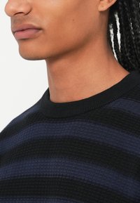 Pull en tricot avec des rayures horizontales bleu foncé et noires, présentant un motif texturé et un col rond côtelé noir uni.