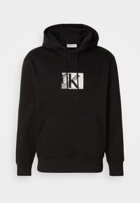 Black hoodie featuring a front kangaroo pocket and a graphic logo in white and gray. Made from soft fabric with a drawstring hood.