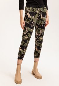 Pantalones jogger con un patrón de camuflaje en verde, negro y beige, con cinturilla elástica y tobillos ceñidos, combinados con botas cortas beige.