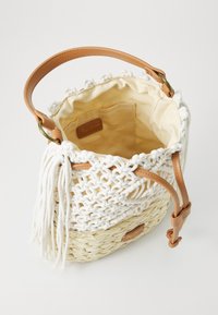 Sac en paille tissé avec un motif blanc crocheté, une lanière en cuir fauve et des détails en franges. Doublure intérieure crème avec une petite poche et une étiquette logo.