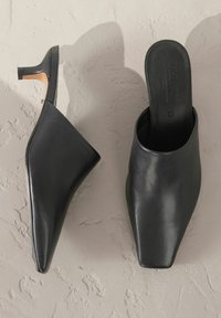 Mulas de cuero negro con punteras puntiagudas y pequeños tacones cuadrados. Textura suave con un diseño elegante. Inscripción en la plantilla: "FIRMADA."
