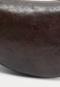Surface en cuir texturé brun foncé avec un texte de marque embossé discret "nice things" près du centre bas.