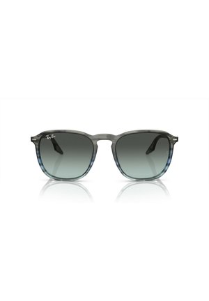 Occhiali da sole trasparenti grigi in plastica con lenti scure a gradiente, forma della montatura quadrata e logo Ray-Ban sull'angolo superiore sinistro della lente.
