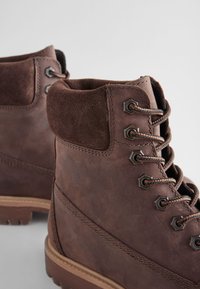 Bottes de randonnée en cuir marron avec accents en daim, œillets métalliques et lacets ronds. Surface texturée et semelle en caoutchouc robuste.