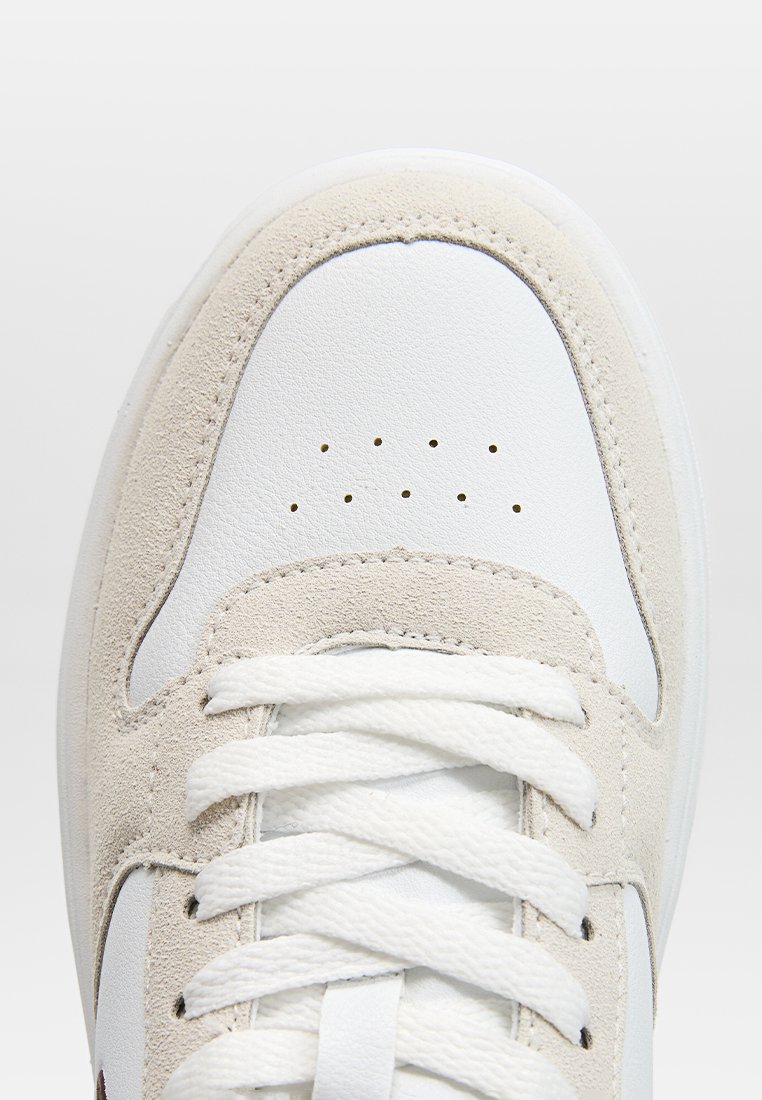 Zapatillas blancas de cuero con acentos de ante beige, puntera redonda, cordones planos blancos y detalles perforados en la caja de los dedos. Superficies suaves y texturizadas.