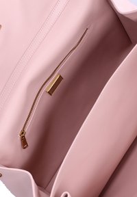 Interno di una borsa in pelle rosa con texture liscia. Caratterizzato da una tasca con zip e hardware dorato e un'etichetta in tessuto. Design pulito e minimale.