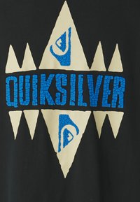 Mustapaita, jossa on suuri sininen ja valkoinen graafinen kuva. Suunnittelussa on kolmiomaisia muotoja ja sana "QUIKSILVER" tekstuurilla sinisellä fontilla.