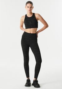Černý sportovní crop top se zipem a odpovídající legíny s vysokým pasem, obojí s opakujícím se textovým vzorem. Měkký, elastický materiál.
