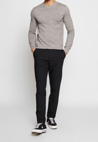 Grå stickad tröja, svarta byxor och svarta sneakers. Outfiten har en enkel design med rund halsringning och en åtsittande silhuett.