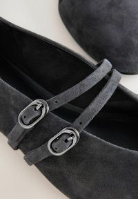 Donkergrijze suède ballerina's met kruisbanden en metalen gespen. Gladde oppervlakte en ronde neus, met interne voering voor comfort.