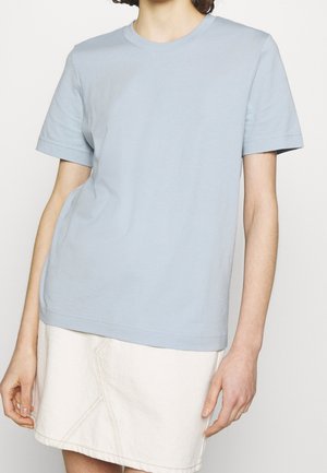 Hellblaue Baumwoll-T-Shirt mit kurzen Ärmeln, rundem Halsausschnitt, lockerer Passform, leicht strukturiertem Stoff, getragen über einem weißen Jeansrock.