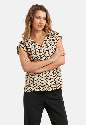 Korte mouwen blouse met een V-hals, voorzien van een crèmekleurig en zwart bladerenpatroon op een lichte stof. Gepaard met zwarte broek.
