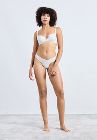 Witte gevoerde beha met verstelbare bandjes en bijpassende hoog uitgesneden bikini slip. Glad textuur, eenvoudig ontwerp, geen zichtbare patronen of accenten.