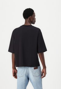 Μαύρο κοντό μπλουζάκι από μαλακό μείγμα βαμβακιού, με κοντά μανίκια και στρογγυλή λαιμόκοψη, συνδυασμένο με ανοιχτό μπλε τζιν παντελόνι.