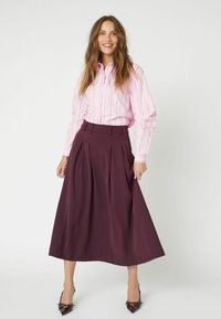 Camicia a righe rosa con bottoni e maniche lunghe abbinata a una gonna di prugna lunga fino al pavimento, con pieghe e vita sagomata. Scarpe con tacco alto.