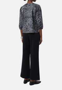Bluse mit Leopardenmuster und Dreiviertelärmeln in Grau und Schwarz, kombiniert mit weiten schwarzen Hosen und flachen schwarzen Schuhen.