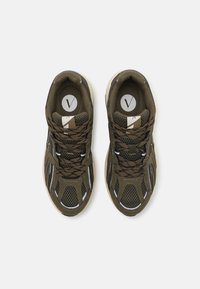 Olive green athletic shoes with mesh and synthetic materials, featuring white accents and brown laces. Round logo on tongue.