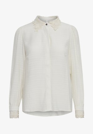 Blouse blanche en tissu texturé, avec un col en dentelle festonné et des accents en dentelle au niveau des poignets. Manches longues et fermeture à boutons.