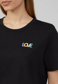 Zwarte katoenen t-shirt met een ronde hals, voorzien van een kleurrijk "LOVE" grafisch logo in pastelkleuren, gepositioneerd op de borst.