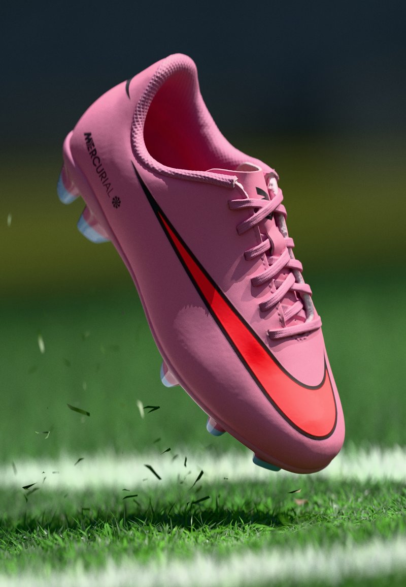 Nike Mercurial jalkapallokengät vaaleanpunaisena, jossa on erottuva musta ja punainen swoosh, varustettuna teksturoidulla päällystyksellä ja läpinäkyvillä piikeillä nurmikolla.