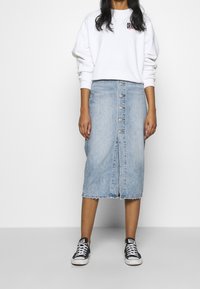 Light blue denim midi skirt with front button closure, frayed hem, paired with a white sweatshirt and black sneakers.