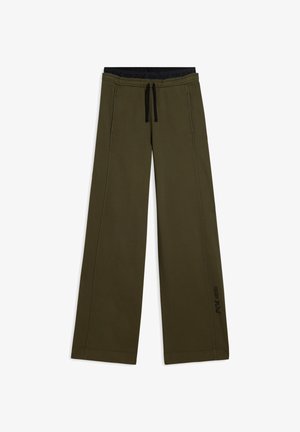 Pantalones de pierna ancha en verde oliva hechos de una tela suave con una cinturilla de cordón, que presentan detalles en negro y un logo estampado en el lateral.