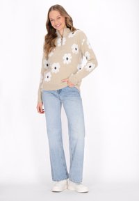 Pulover tricotat bej cu modele florale albe și bițe întunecate, guler cu jumătate de fermoar. Asortat cu blugi evazați albaștri deschiși și adidași albi.