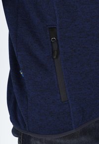Maglione in blu navy con tasca laterale con zip e finiture nere. Il tessuto testurizzato e il dettaglio a contrasto dell'orlo completano il design.