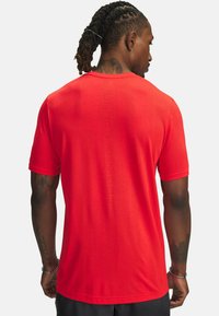 T-shirt sportivo rosso a maniche corte, tessuto testurizzato e un dettaglio di branding discreto sul retro. Design leggero e traspirante.