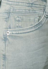 Ljusblå denimjeans med en framficka, subtil textur och kontrasterande sömmar. Silvrig detaljer vid fickan.