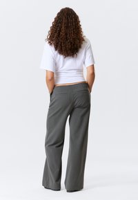 Pantalons larges gris à rayures, dotés de poches arrière. Assortis avec un t-shirt court blanc, présentant un design simple.