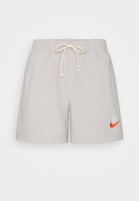 Light grey swim shorts with a checkered pattern, elastic waistband with drawstring, and an orange Nike logo on the lower left side.