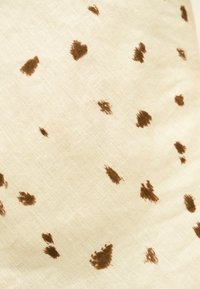 Tissu crème avec des taches irrégulières brun foncé éparses ressemblant à un motif animal abstrait ou à des éclaboussures de peinture.