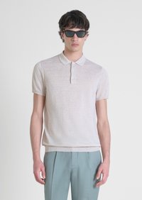 Polo shirt beige chiaro a maniche corte in maglia texturizzata con colletto e tre bottoni. Abbinato a pantaloni su misura azzurro chiaro.