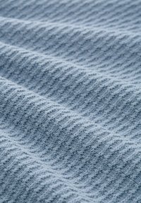 Lichtblauwe gebreide stof met een gestructureerd, geribbeld patroon. Het materiaal lijkt zacht en gezellig, met duidelijke afwisselende verheven en platte secties.