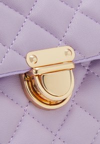 Borsa a tracolla in pelle trapuntata color lavanda con chiusura rotonda dorata e dettagli di cucitura, caratterizzata da una texture liscia e un motivo geometrico.