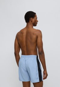 Ανοιχτό γαλάζιο μαγιό σορτς με μαύρες πλαϊνές πιέτες, ελαστική μέση και άνετη εφαρμογή. Κατασκευασμένο από λείο, ελαφρύ ύφασμα.