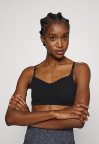 Bralette preto com um design em V e alças finas. Tecido suave com um estilo ajustado, combinado com leggings cinzentas estampadas.