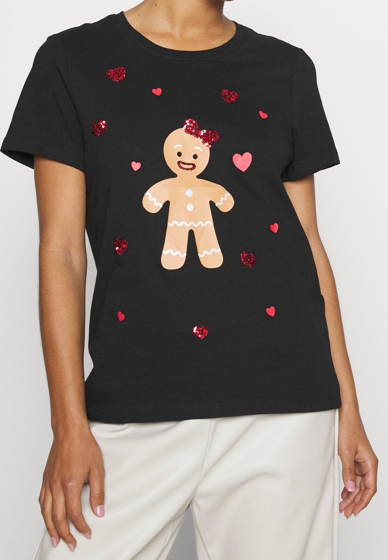 T-shirt noir avec une figure centrale de pain d'épices portant un nœud rouge, entourée de formes de cœur rouges et roses scintillantes.