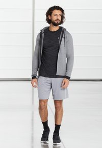 Meeste spordirõivastus, mis sisaldab halli tõmbluku hoodiea, musta lühikese varrukaga särki ja halli lühikesed pükse. Mustad tossud täiustavad välimust.